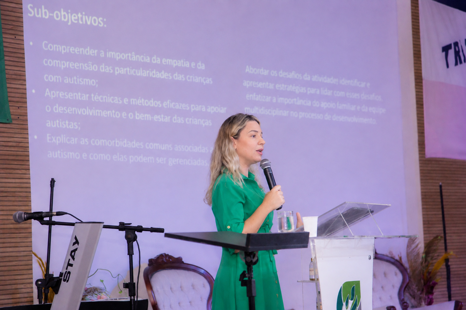 Lorena Jacob ministrando uma palestra com microfone diante de uma apresentação projetada