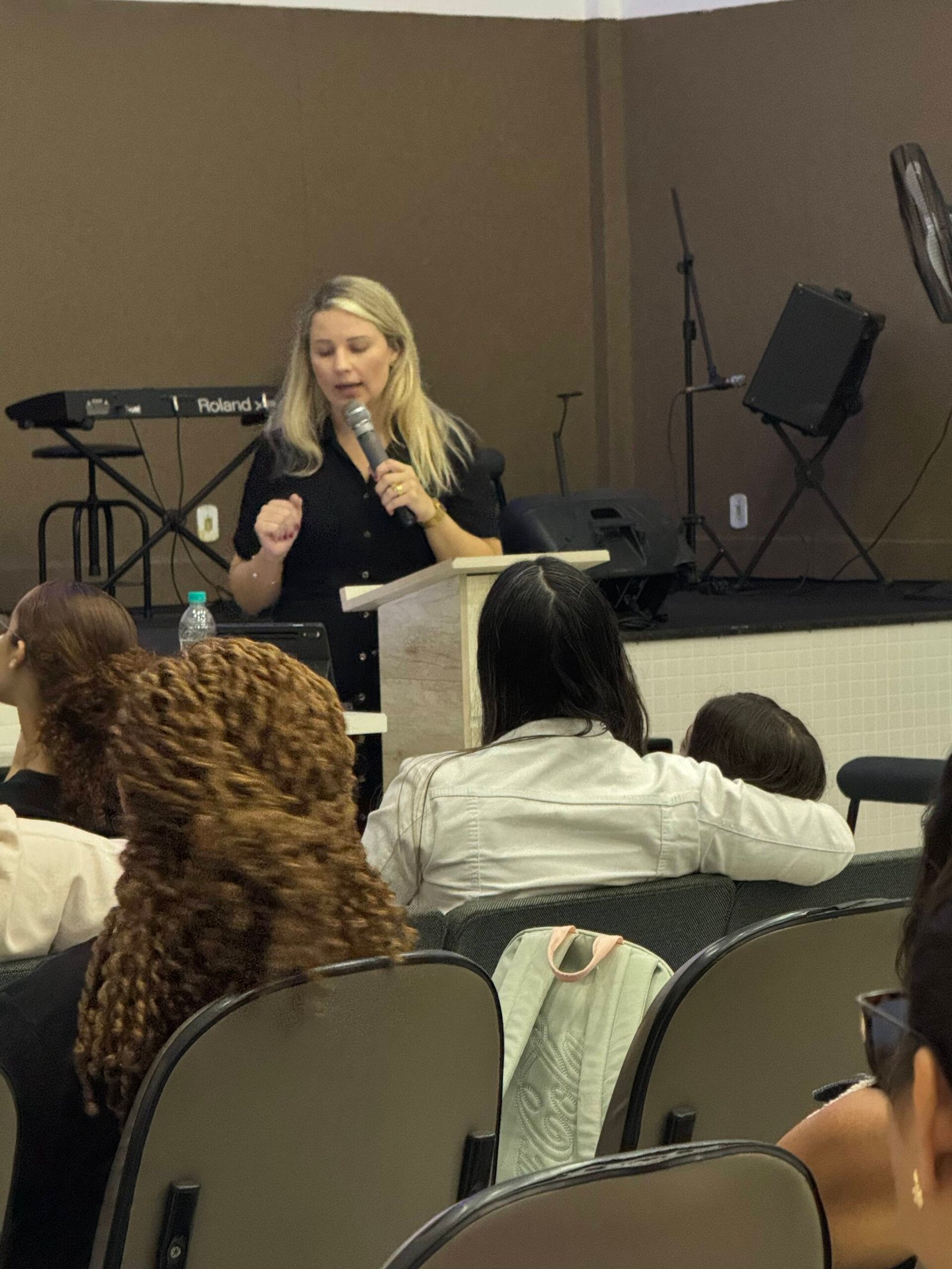 Lorena Jacob falando ao microfone durante uma palestra presencial